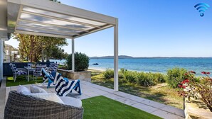 A covered outdoor seating area with a view of the sea, a pergola, and a wicker chair.