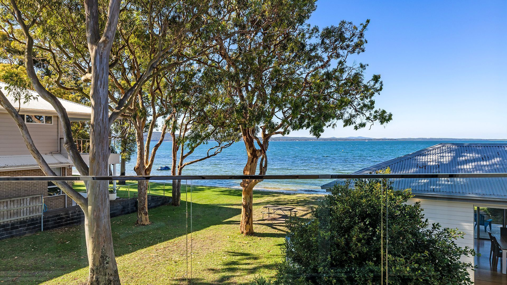 A view of a coastal property with a grassy lawn, a picnic table, and a metal fence.