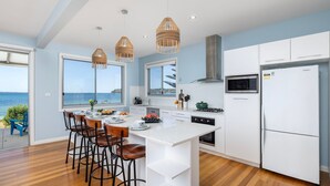 A modern kitchen with a large island, bar stools, and a view of the sea.