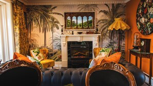 A living room with a fireplace, a large painting of palm trees, and a tropical mural. - Lore Haven - Your little slice of paradise (Robe)