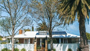 A two-story house with a white exterior, a brick chimney, and a solar panel on the roof. - Lore Haven - Your little slice of paradise (Robe)