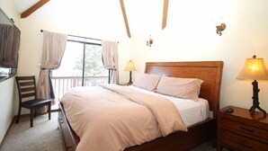 Ein Schlafzimmer mit einem hölzernen Bett, einem Sessel, einem Nachttisch und einem Fenster mit Vorhängen.