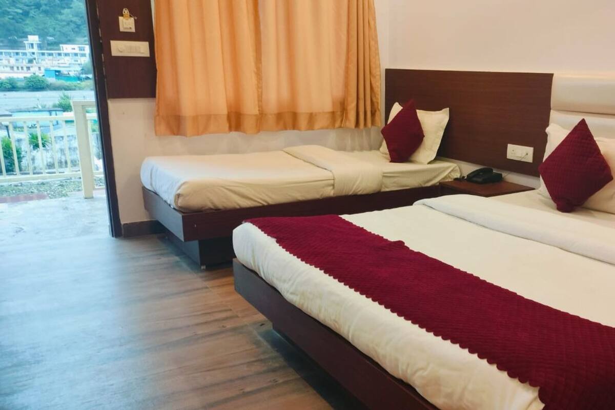 A hotel room with two beds, a wooden floor, a view of the outside, and a window with curtains.