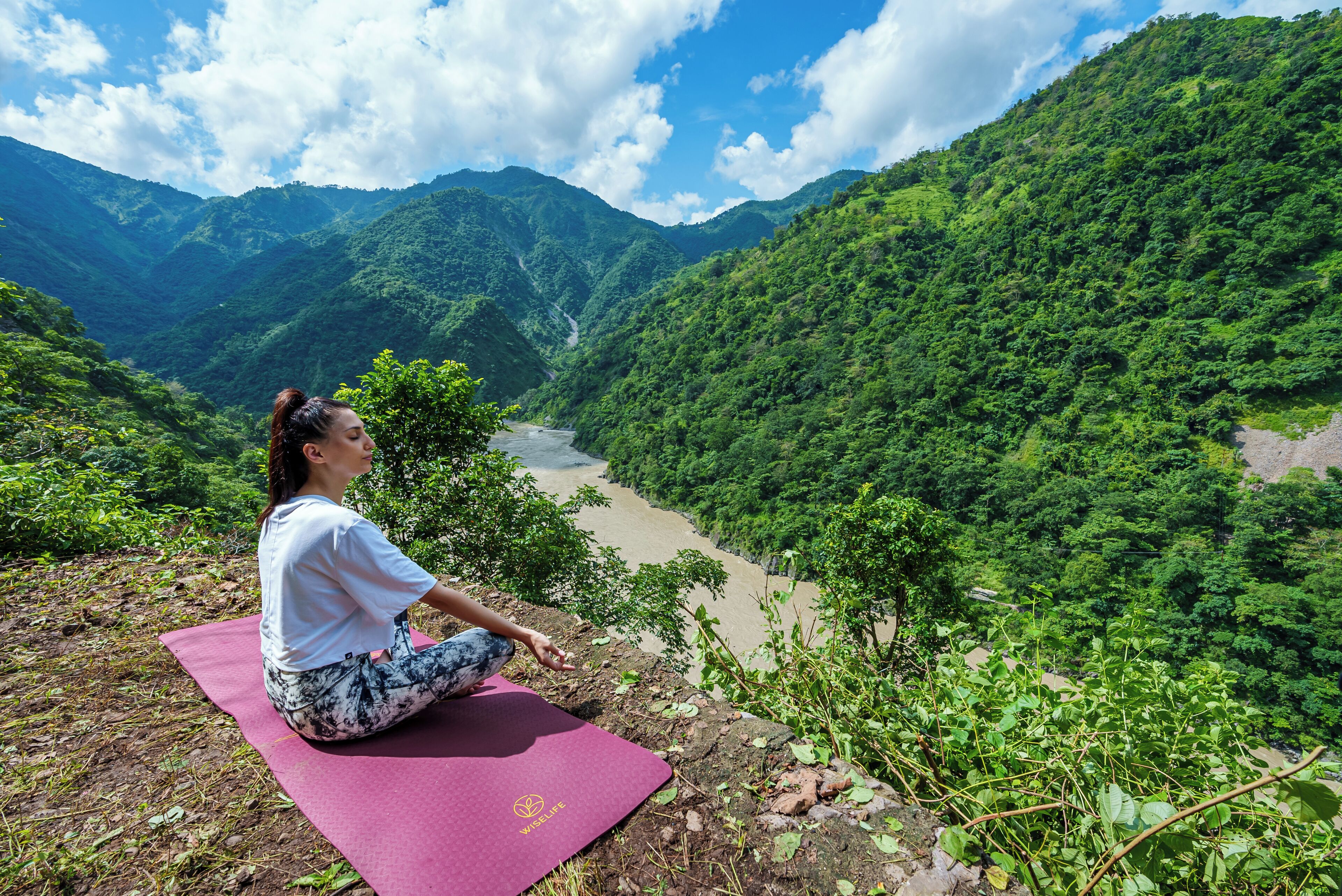 A person meditating on a red mat with a view of a river and mountains.