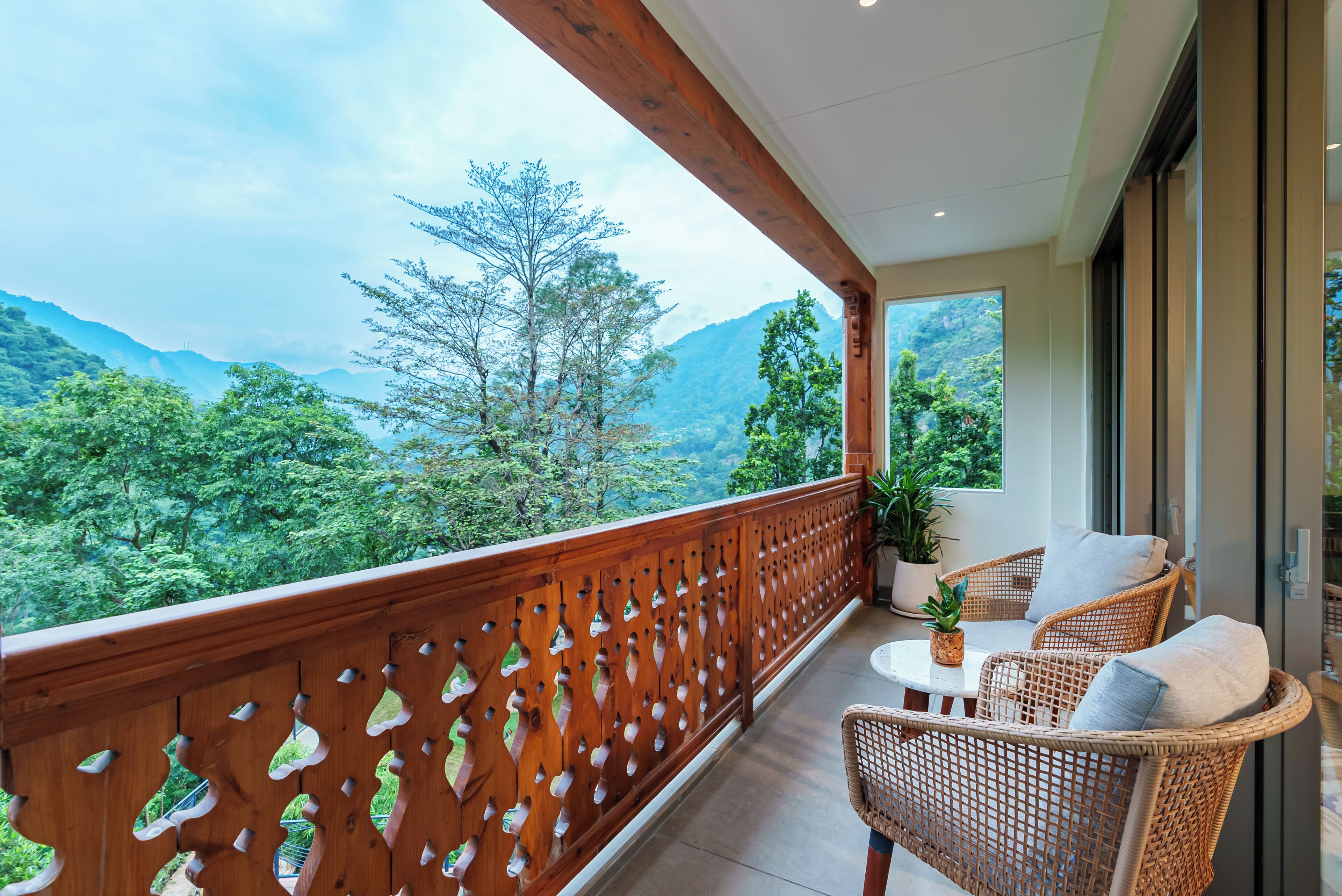 A balcony with wicker furniture, a potted plant, and a view of a mountainous landscape.
