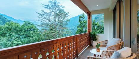 A balcony with wicker furniture, a potted plant, and a view of a mountainous landscape.