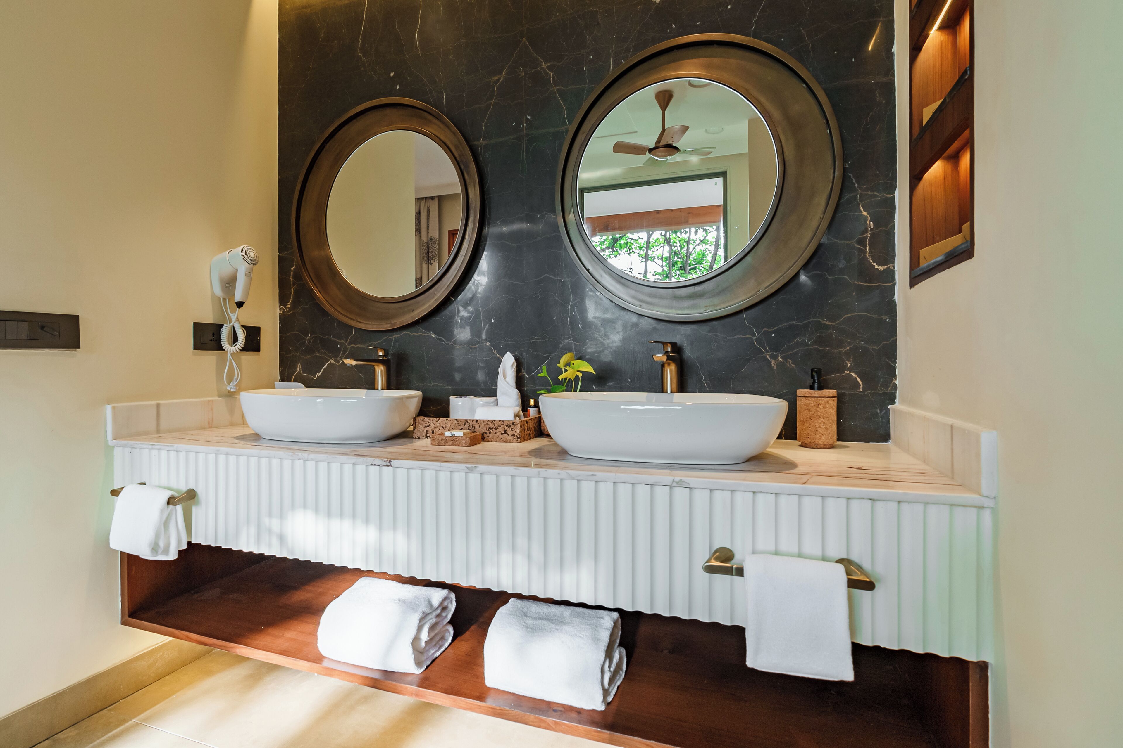 A bathroom with two round mirrors, a white sink, and a wooden vanity.
