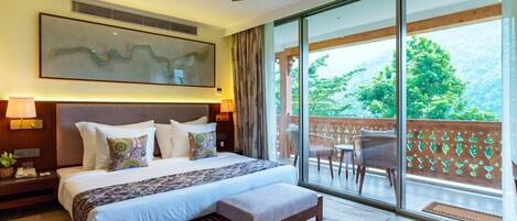 A modern hotel room with a large bed, a ceiling fan, a balcony with a view of greenery, and a large window.