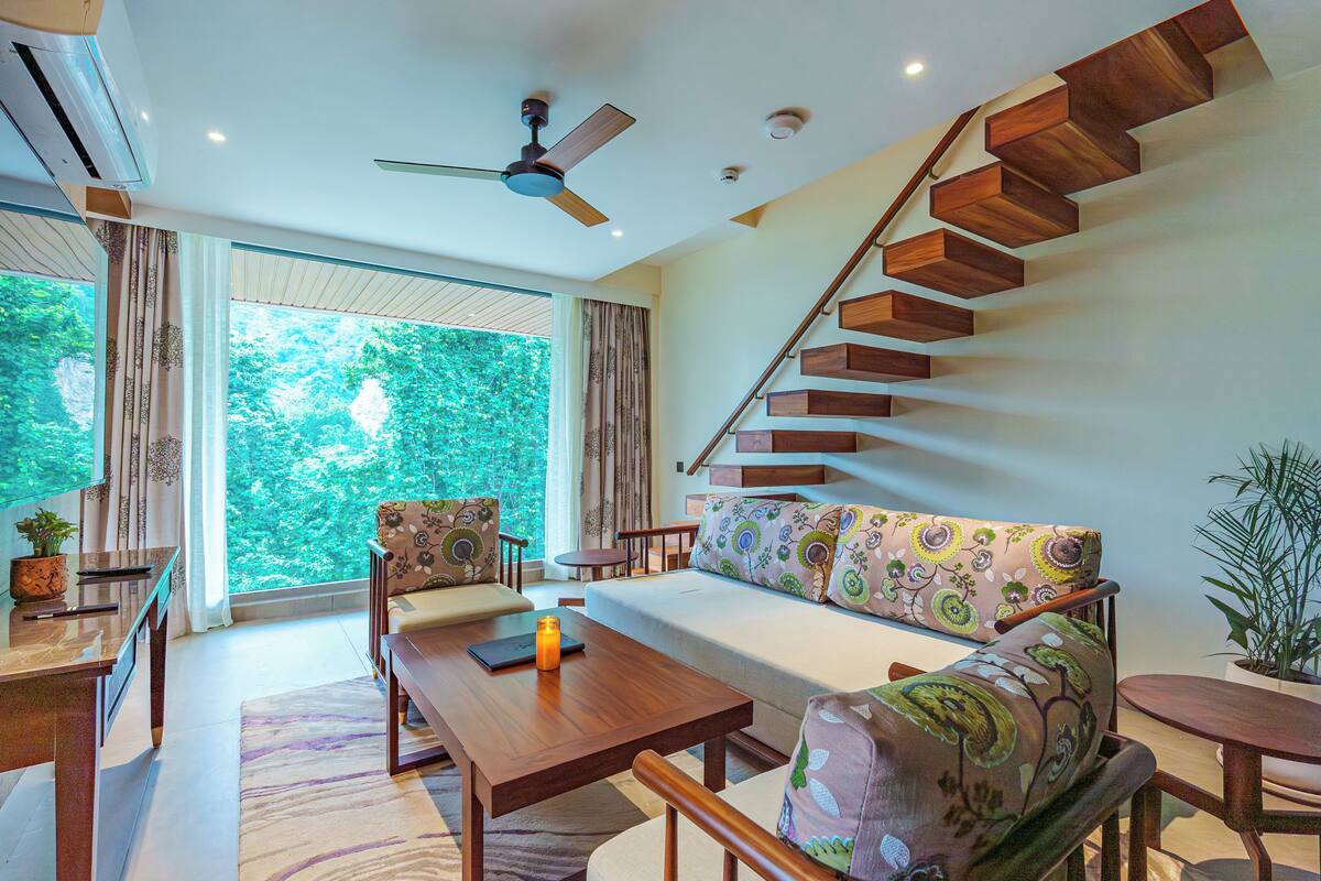 A modern living room with a wooden staircase, a sofa, a coffee table, and a dining area.
