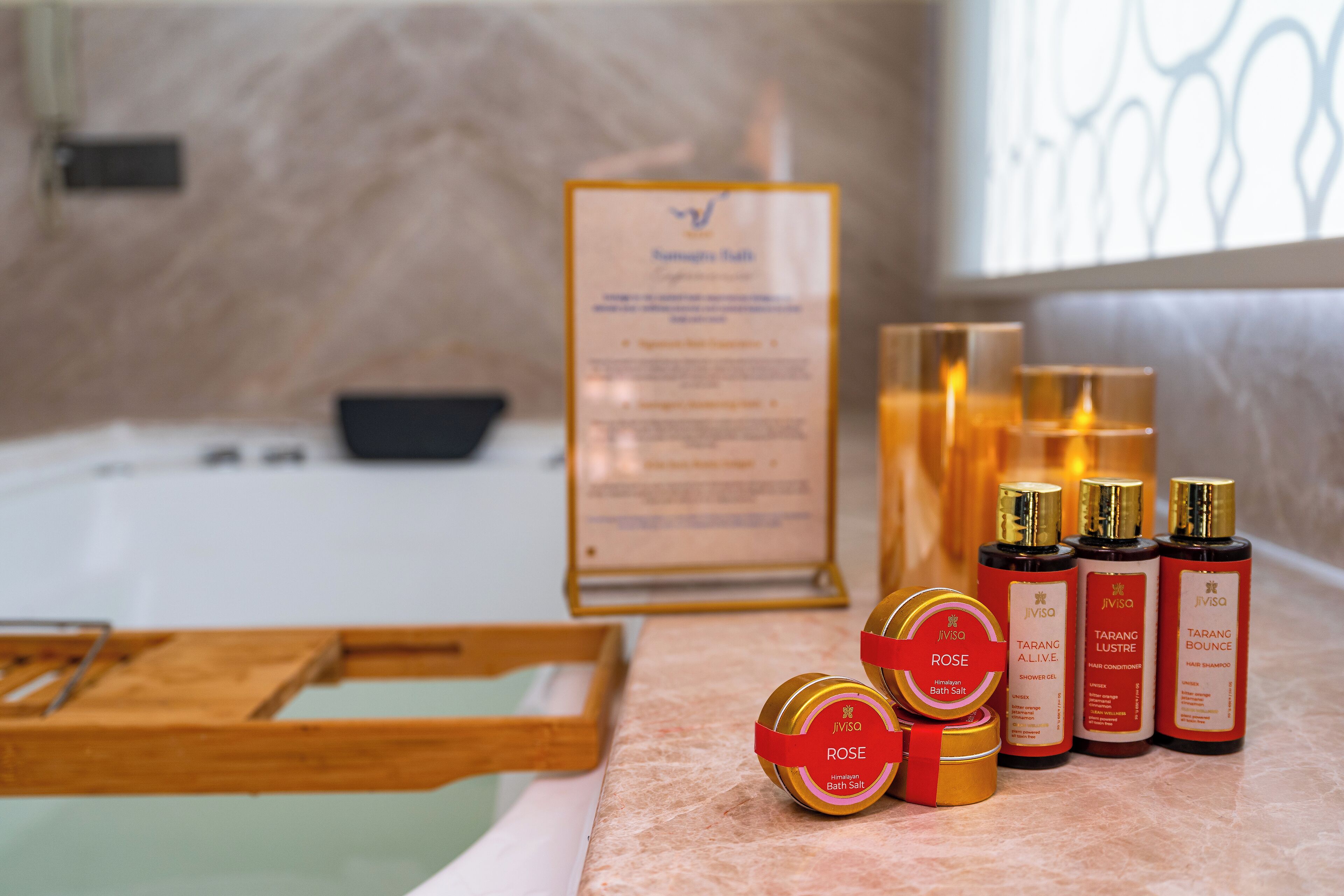 A bathroom with a bathtub, a wooden tray, and various toiletries including a bath salt container, a shower gel, and two hair care products.