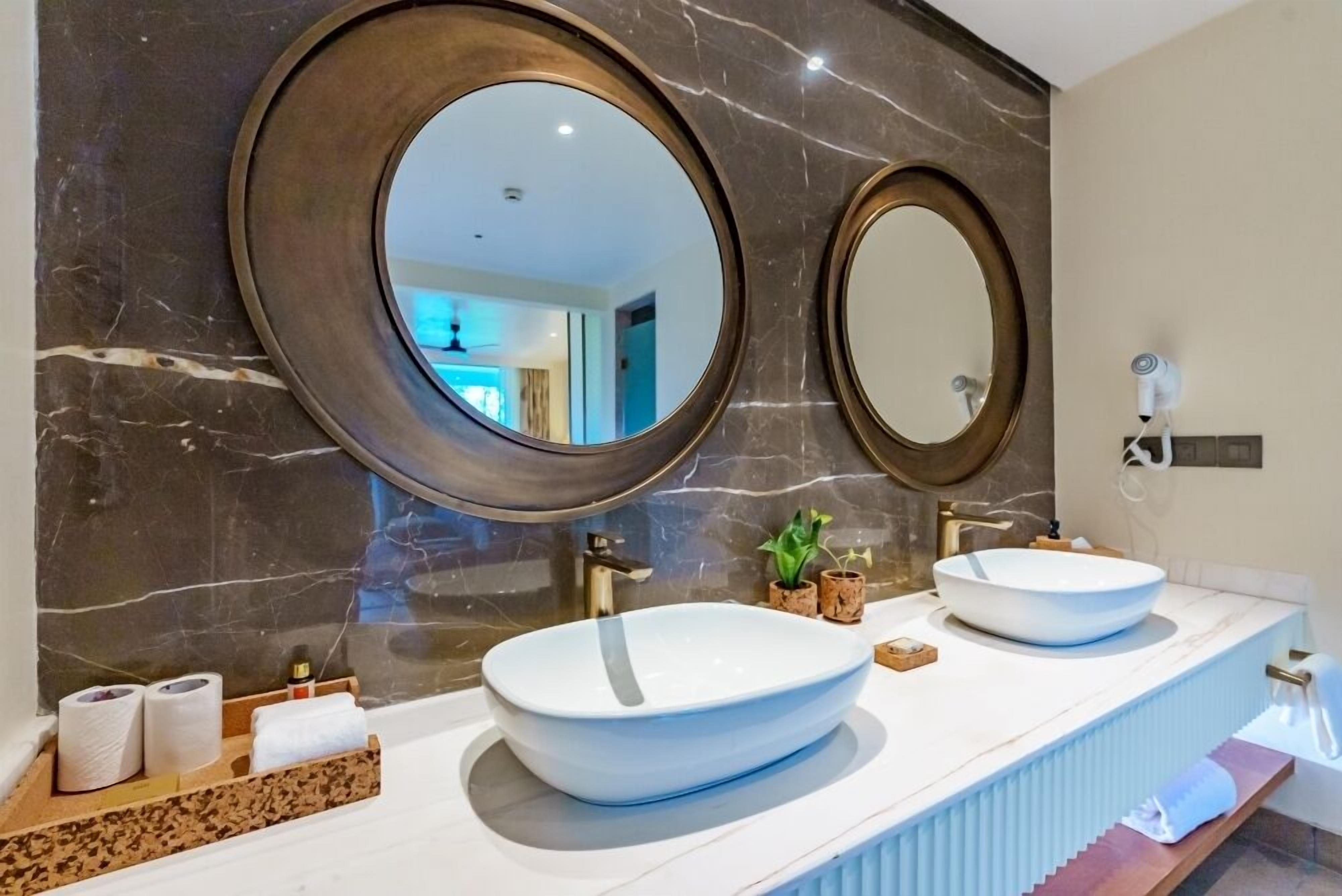 A modern bathroom with two oval sinks, large mirrors, and a marble backsplash.