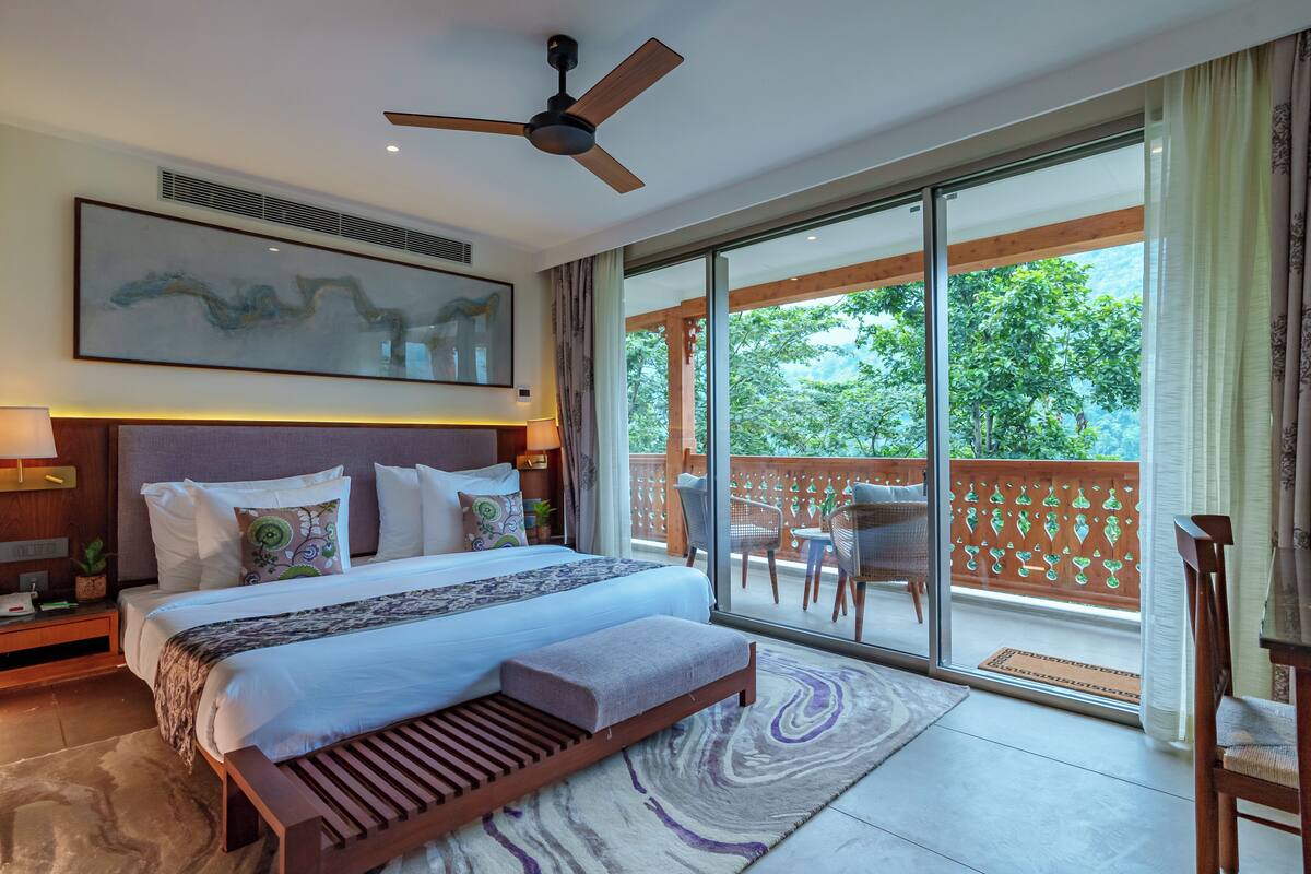A spacious bedroom with a large bed, a ceiling fan, a view of the outdoors, and a balcony with furniture.