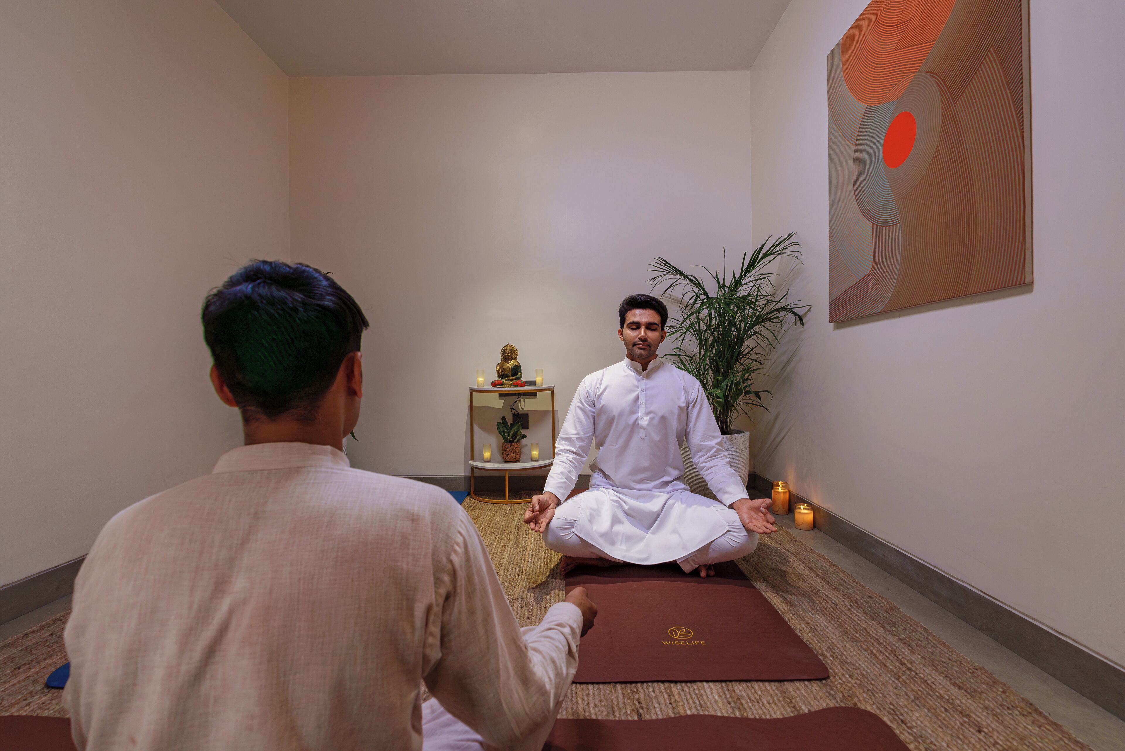 A meditation room with a person sitting cross-legged on a mat, a statue, and a plant.