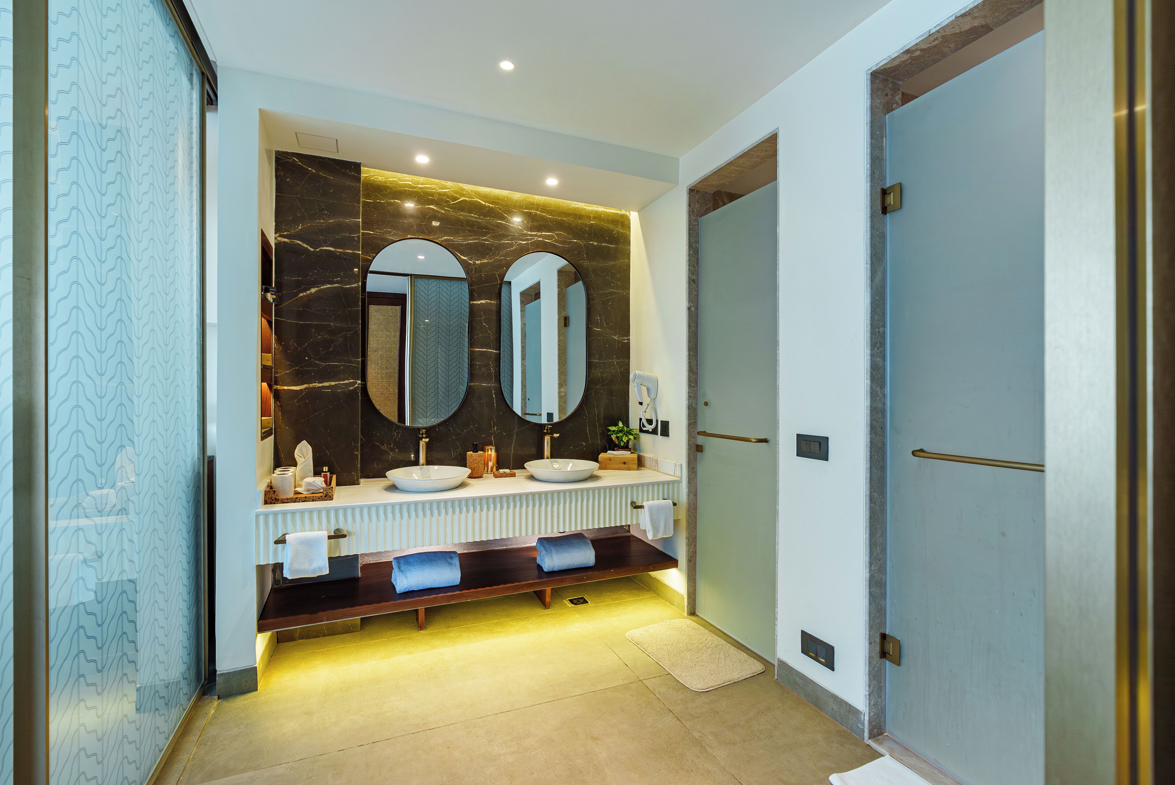 A modern bathroom with a marble vanity, dual sinks, and a bench with towels.