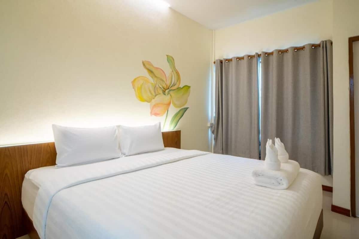 A hotel room with a bed, pillows, a painting of flowers, curtains, and a towel on the bed.
