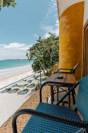 A beachside balcony with wicker furniture, a wooden table, and a view of the ocean.