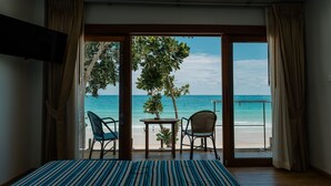 A room with a bed, a table, two chairs, and a view of the beach and ocean through a glass door.