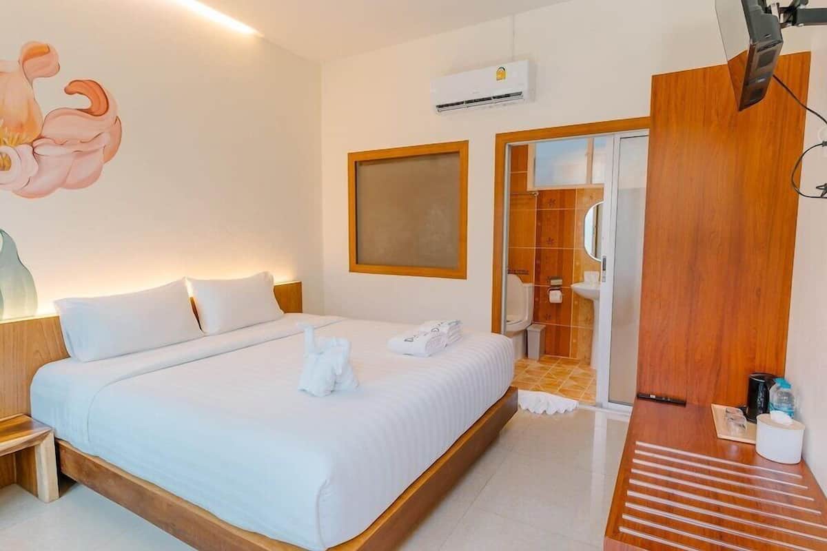 A hotel room with a bed, a wooden headboard, an air conditioning unit, a wooden door, and a small table with a cup and tissues.