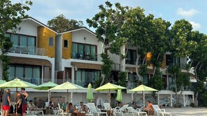 A beachfront hotel with multiple balconies, outdoor seating areas with umbrellas, and a sandy beach.