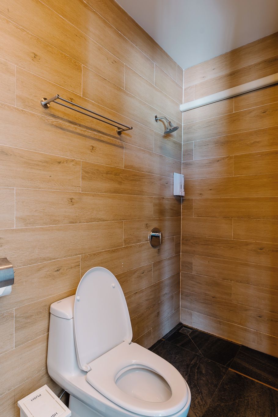 Une salle de bain moderne avec un mur en bois, des toilettes blanches, un porte-serviettes et un espace douche.