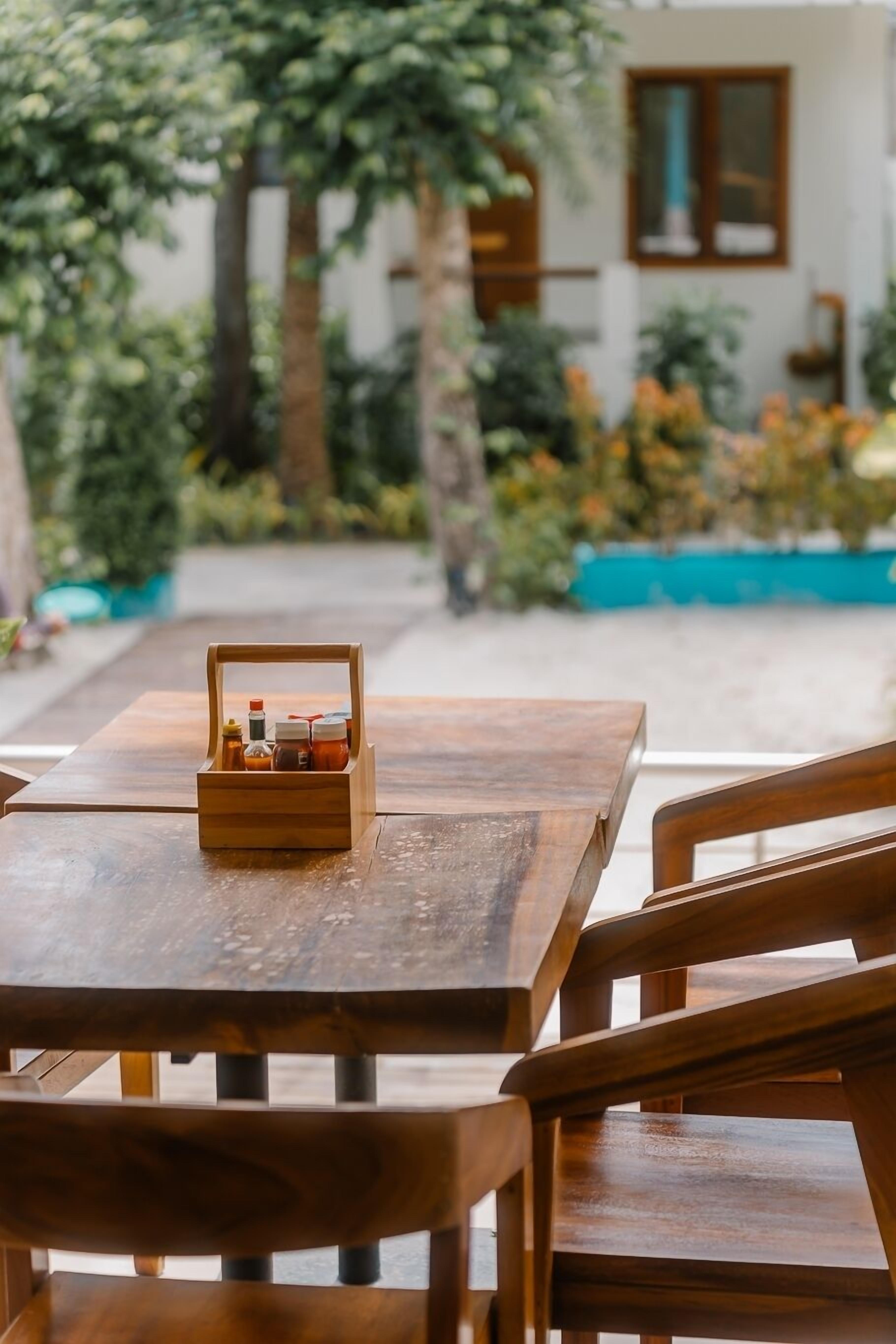 A wooden table with a small wooden box containing bottles, set on a patio with a view of a building and greenery in the background.
