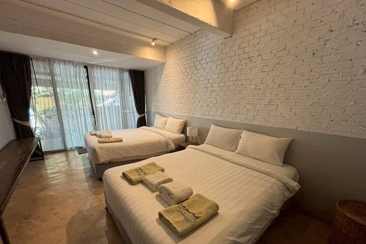 A hotel room with two beds, white linens, and a brick wall.