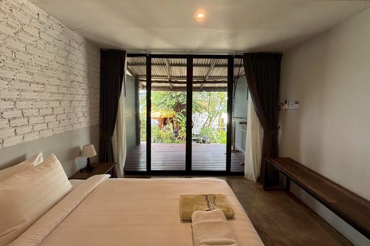 A hotel room with a large bed, a bench, and a view of a garden through a sliding door.