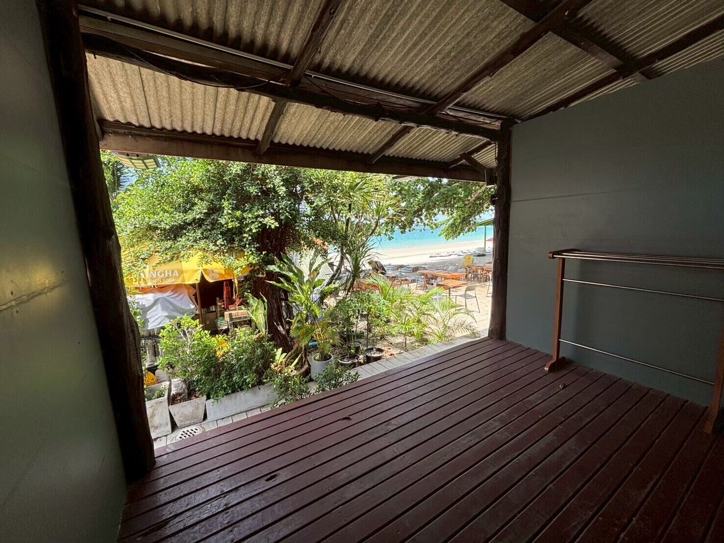 Una terraza de madera con barandilla metálica, con vista a una playa y un pequeño espacio exterior con una sombrilla amarilla.