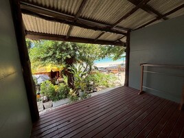 A wooden deck with a metal railing, overlooking a beach and a small outdoor seating area with a yellow umbrella.