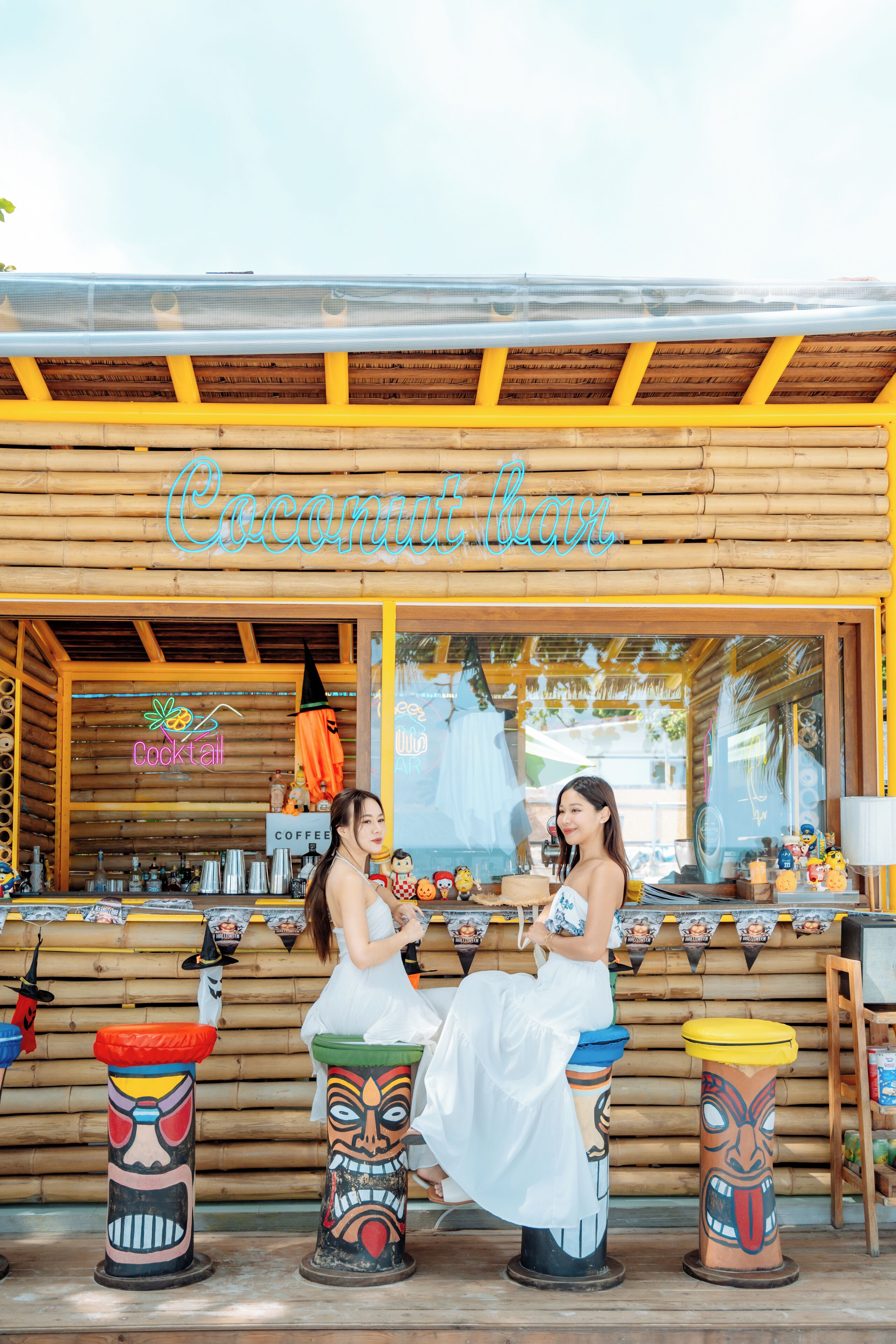 A wooden bar with a tropical theme, including tiki totems and a neon sign reading "Coconut bar".