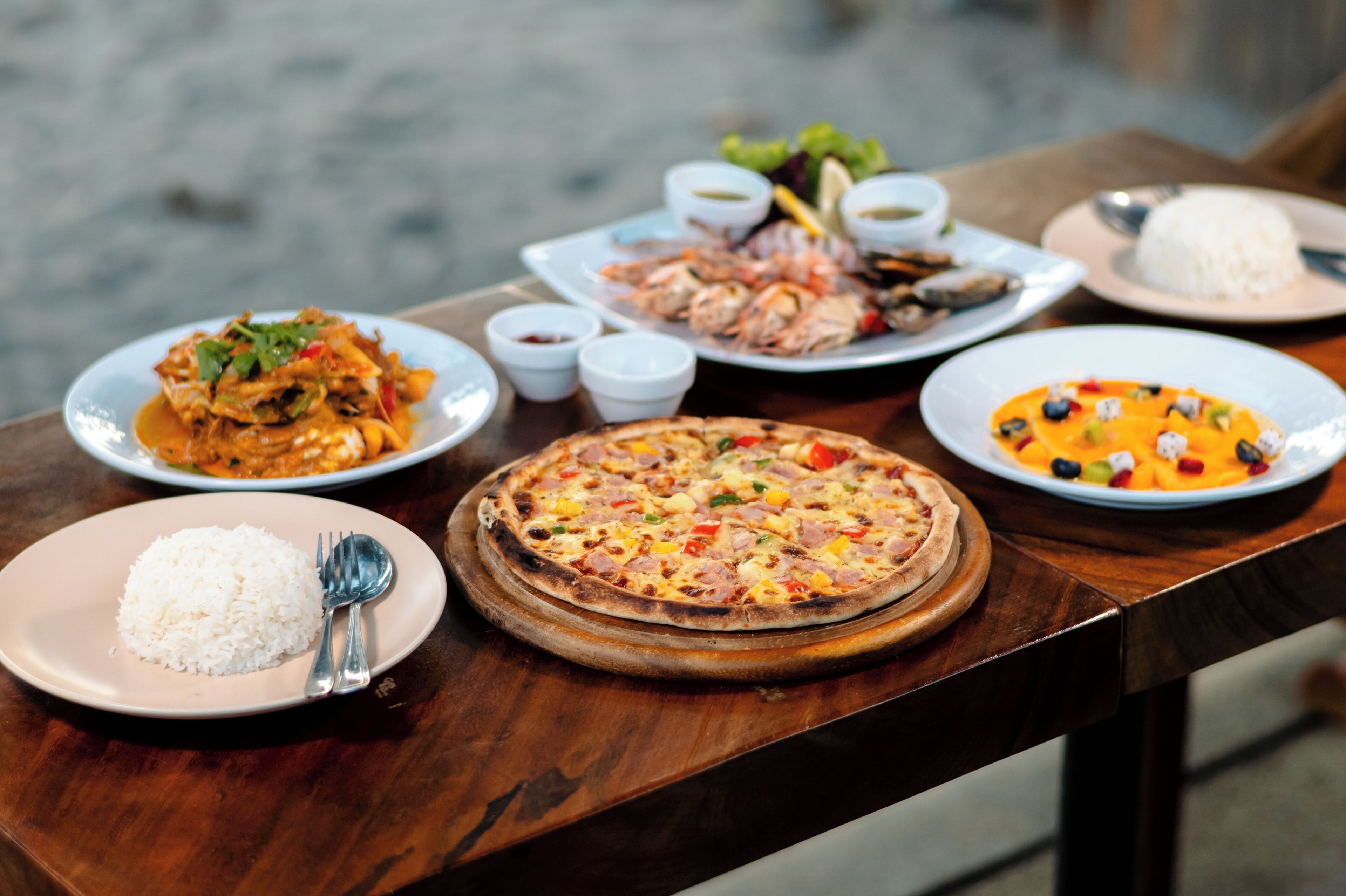 A wooden table with various dishes including rice, shrimp, and a pizza.