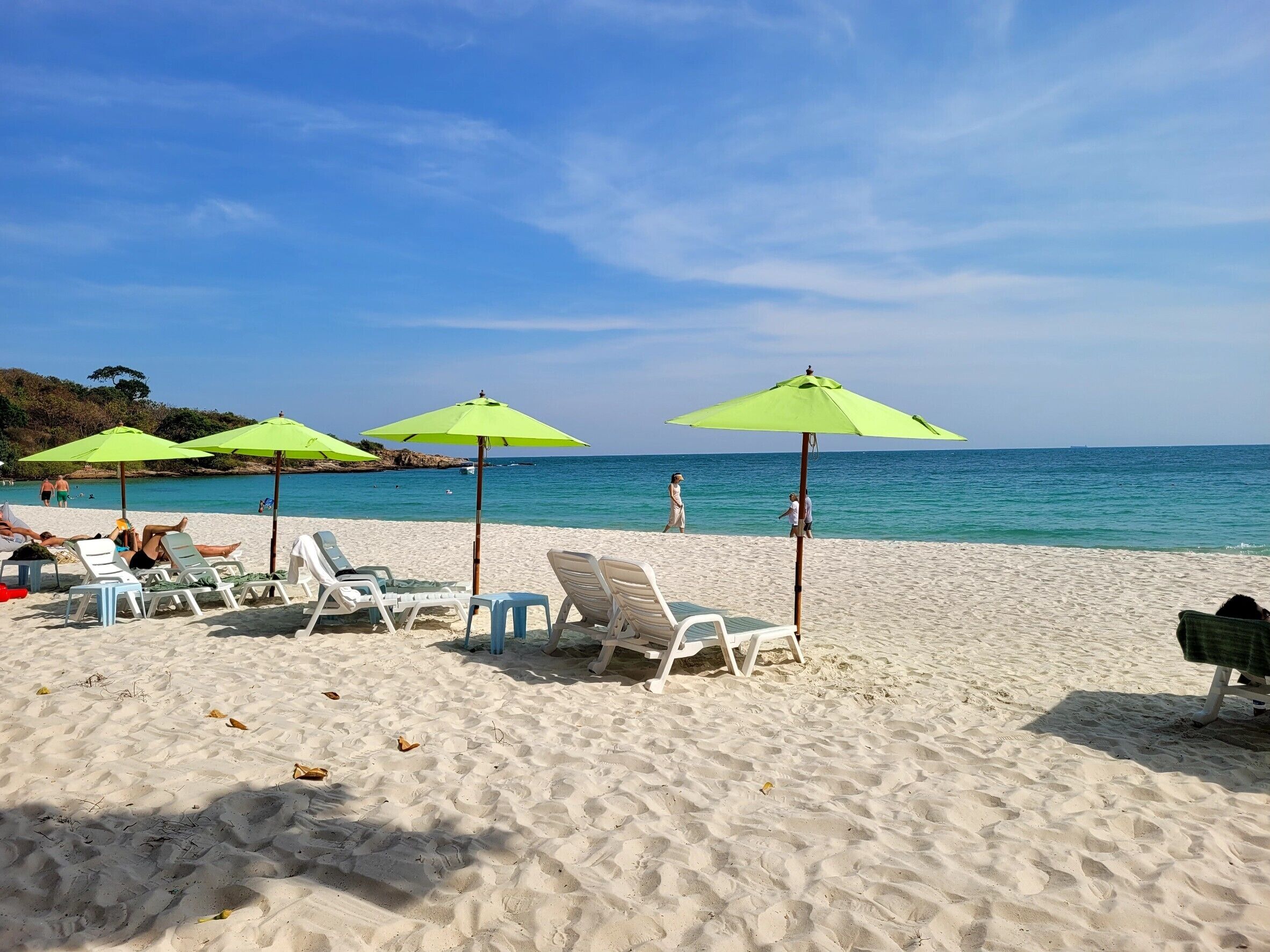 A beach with white lounge chairs and green umbrellas, a clear sky, and calm sea.
