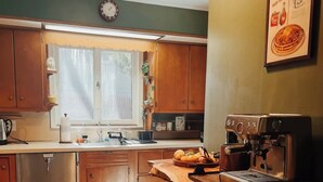 A kitchen with wooden cabinets, a stainless steel refrigerator, a coffee machine, and a window with curtains.