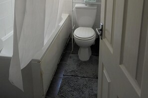 A narrow bathroom with a white toilet, a white bathtub, and a dark floor. - Leeds - Apartment - Stay 3- Parking - Garden (Leeds)