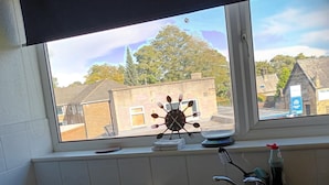 A kitchen with a window view of a town, a clock with utensils, and a sink with a toothbrush. - Leeds - Apartment - Stay 3- Parking - Garden (Leeds)