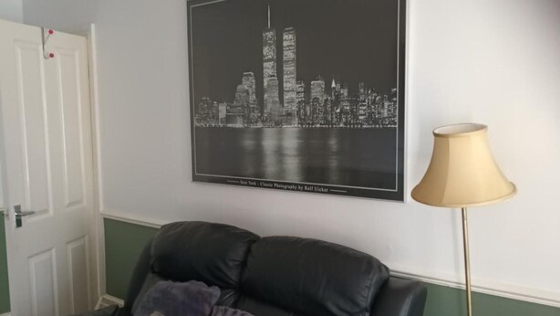 A room with a black and white cityscape photograph on the wall, a black leather sofa, and a floor lamp. - Leeds - Apartment - Stay 3- Parking - Garden (Leeds)