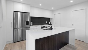 Una cocina moderna con armarios blancos, un refrigerador de acero inoxidable, un salpicadero oscuro y una isla de encimera blanca.