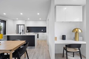 A modern kitchen with white cabinetry, a central island, and a dining area with a wooden table and chairs.