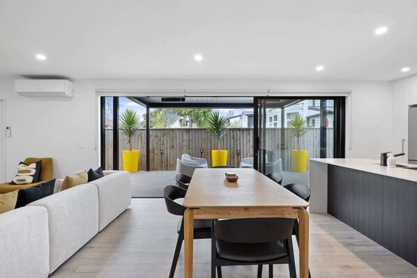 A modern living room with a sofa, dining table, chairs, and a kitchen area.