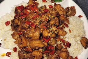Un plato de comida con arroz y un guiso de carne, posiblemente pollo, adornado con chile rojo y nueces.