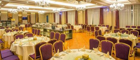 A banquet hall with round tables, purple chairs, and chandeliers.