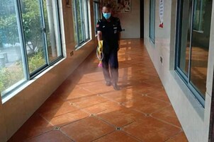 Un pasillo con ventanas amplias, piso de baldosas y una persona cargando un utensilio de limpieza.