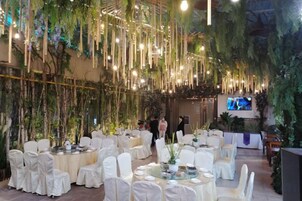 Un salón de banquetes con mesas redondas, sillas blancas y plantas colgantes.