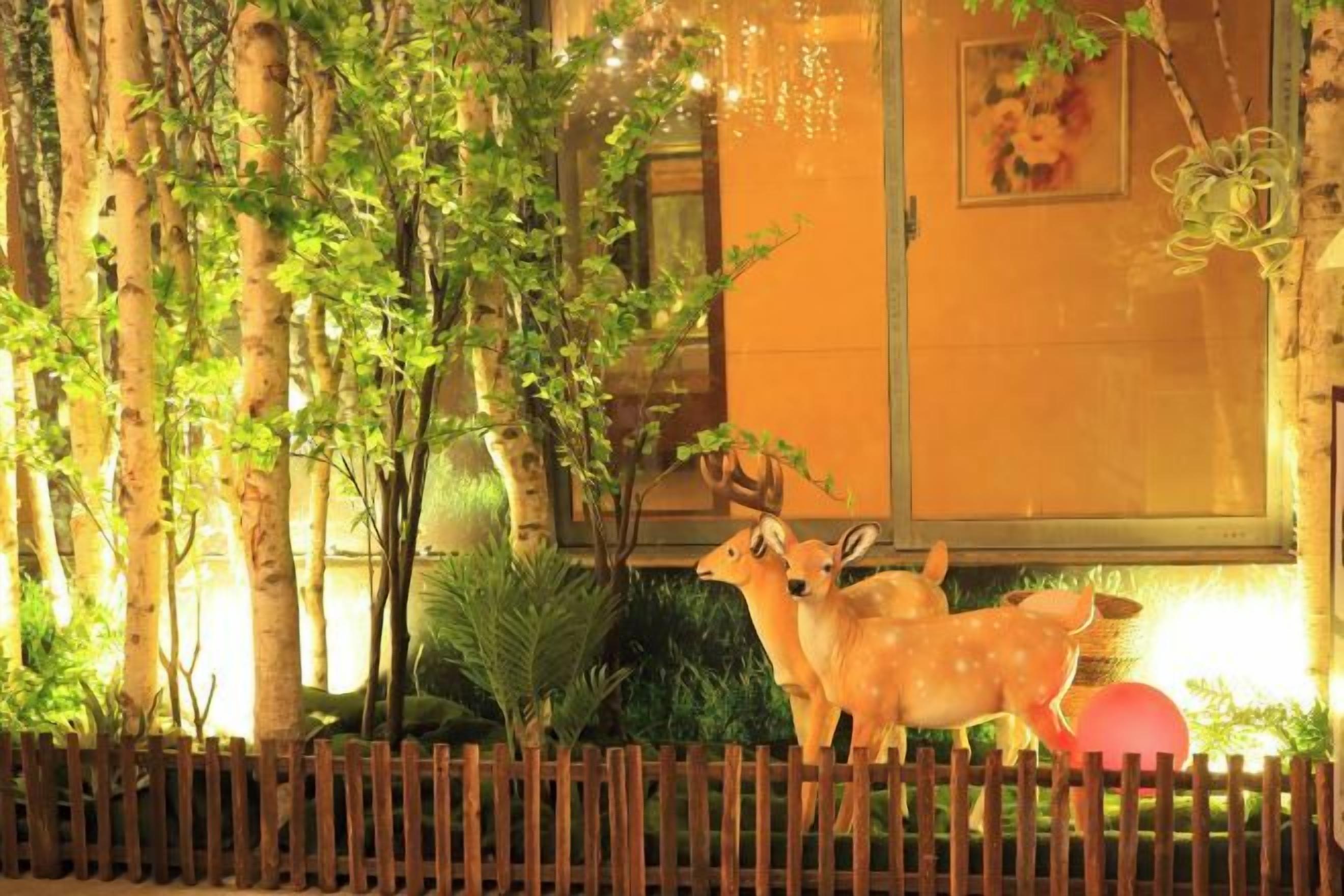 A decorative outdoor area with a wooden fence, trees, and a statue of deer.