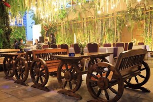 Mobiliario exterior con mesas y bancos de madera, rodeado de plantas colgantes y follaje.