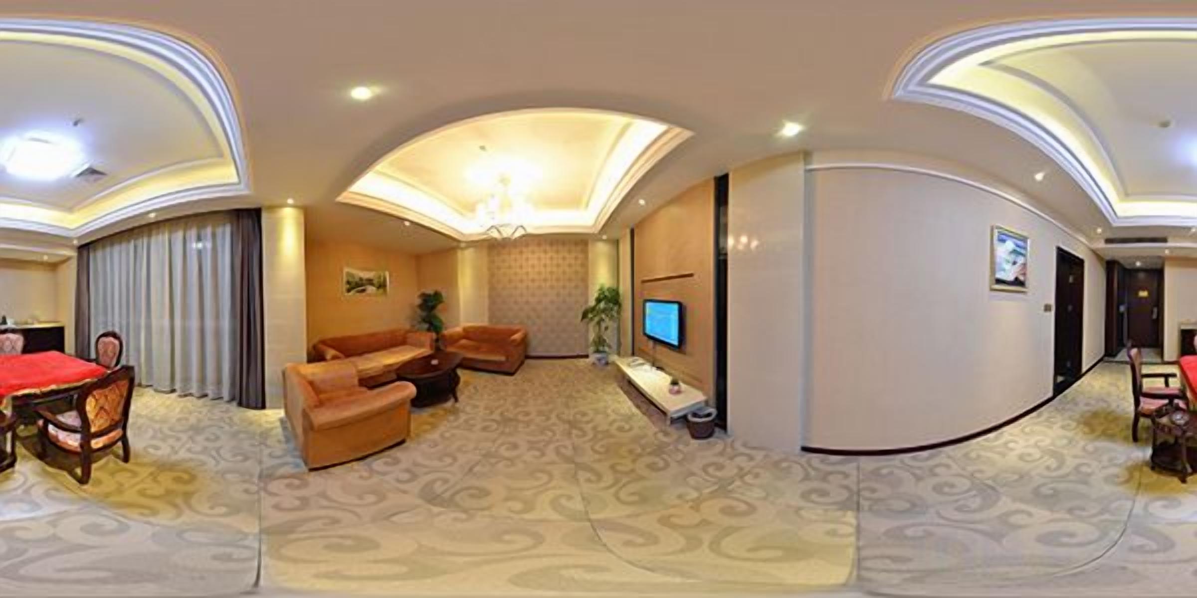 Habitación de hotel con comedor, un conjunto de sofás, televisión y piso alfombrado.