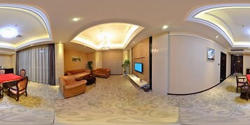 Habitación de hotel con comedor, un conjunto de sofás, televisión y piso alfombrado.