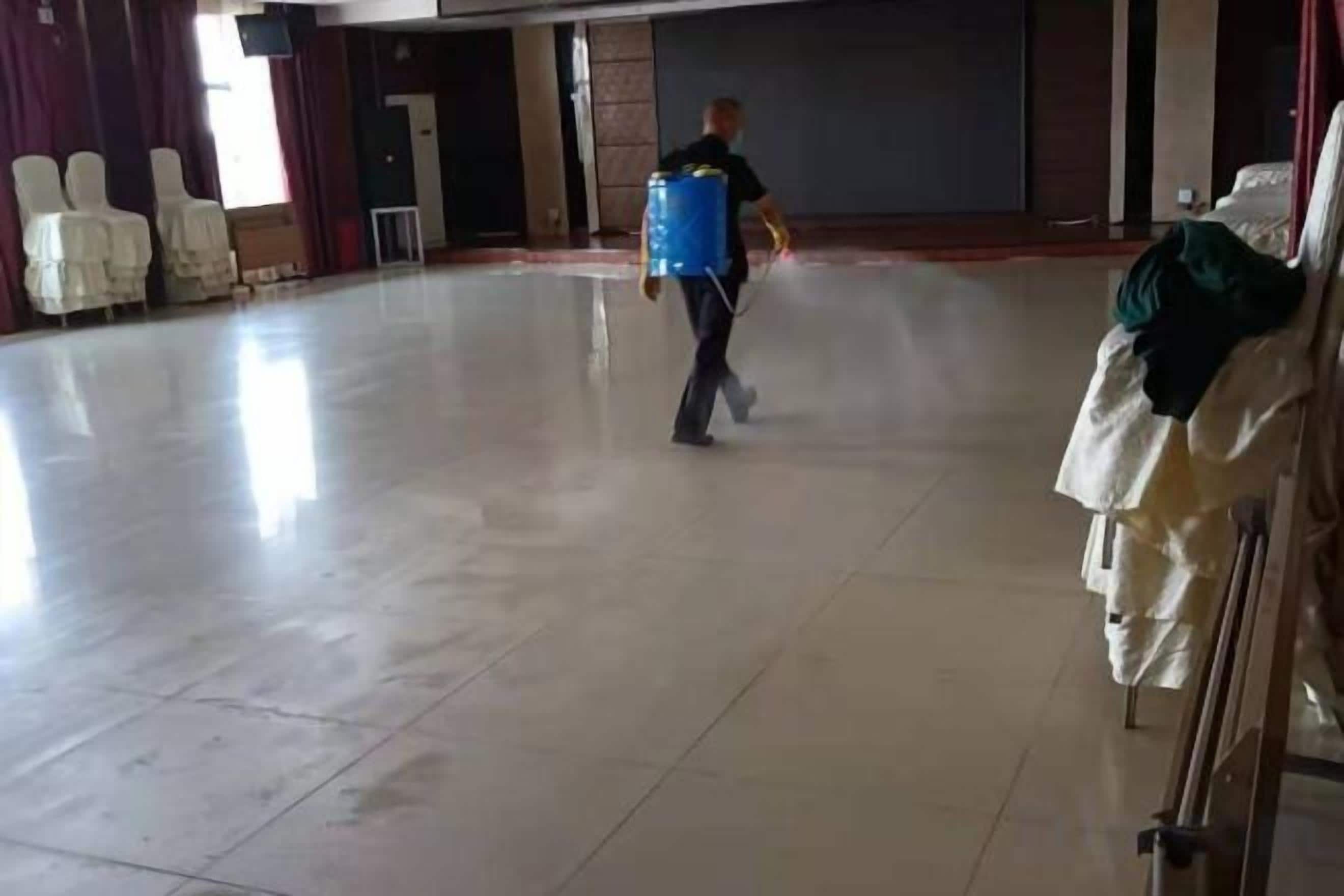A spacious indoor area with a tiled floor, rows of white chairs, and a person carrying a blue container.
