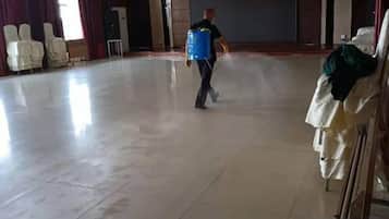 A spacious indoor area with a tiled floor, rows of white chairs, and a person carrying a blue container.