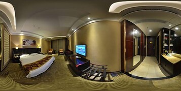 Habitación de hotel con cama, televisión, zona de estar y espejo.